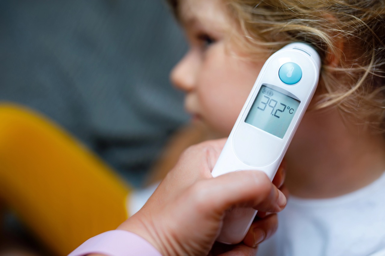 Mother takes temperature for her little preschool daughter, sick child with infrared in ear thermometer at home, high grade fever Mother hand holding digital infrared thermometer.